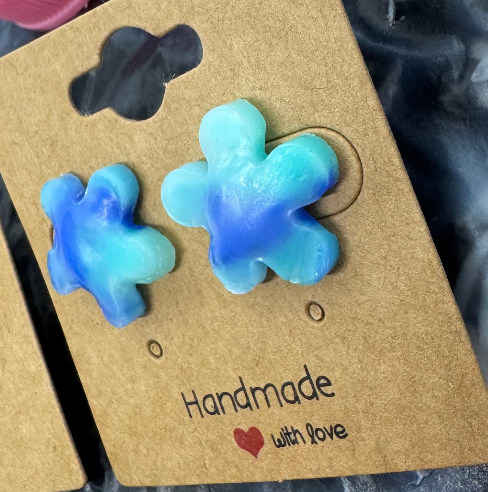Flower-shaped earrings on a cardboard backing with colorful bottle caps in the background.