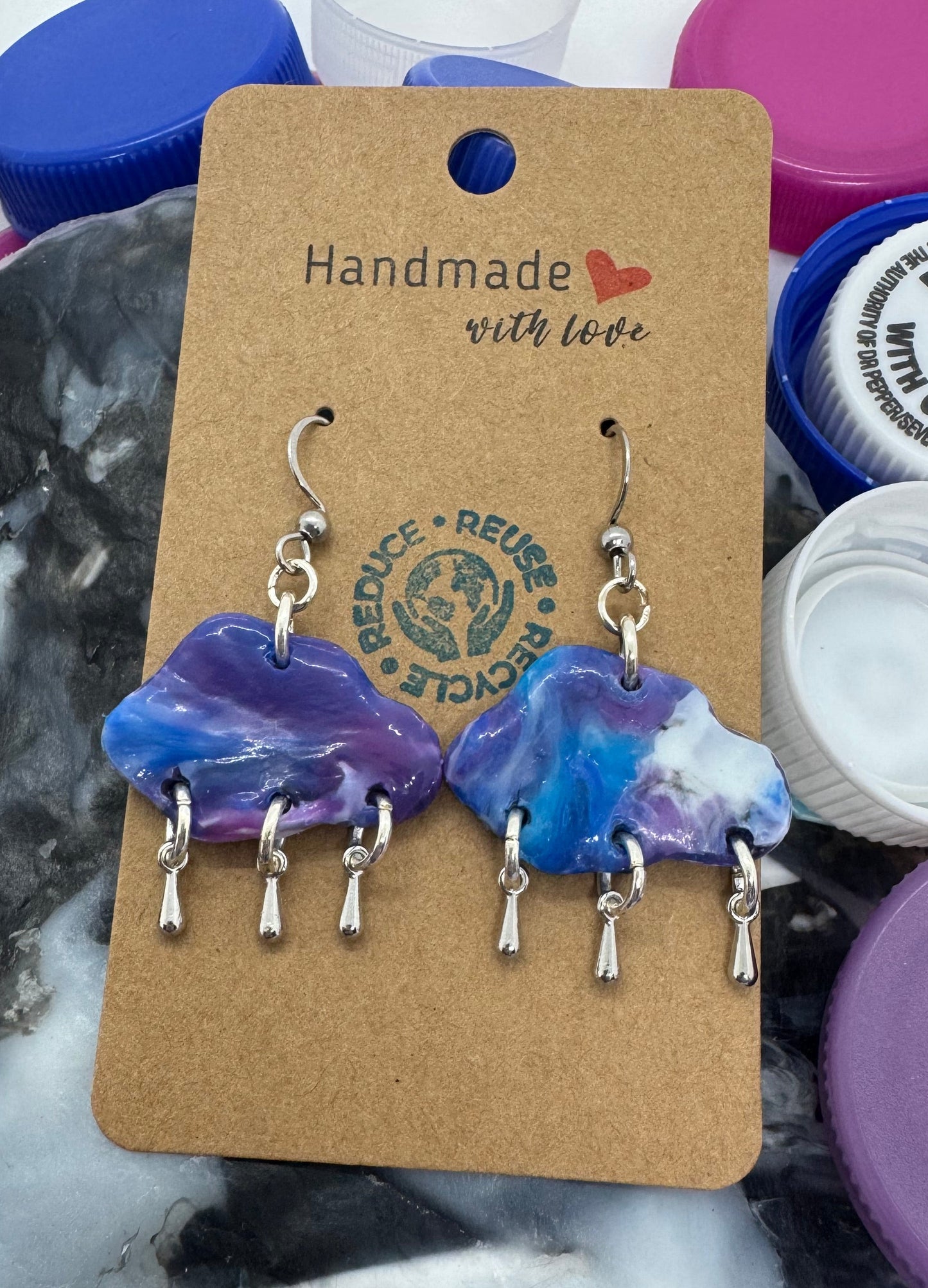 Set of earrings on a cardboard card with a 'Handmade with Love' tag, surrounded by colorful bottle caps.