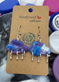 Set of earrings on a cardboard card with a 'Handmade with Love' tag, surrounded by colorful bottle caps.