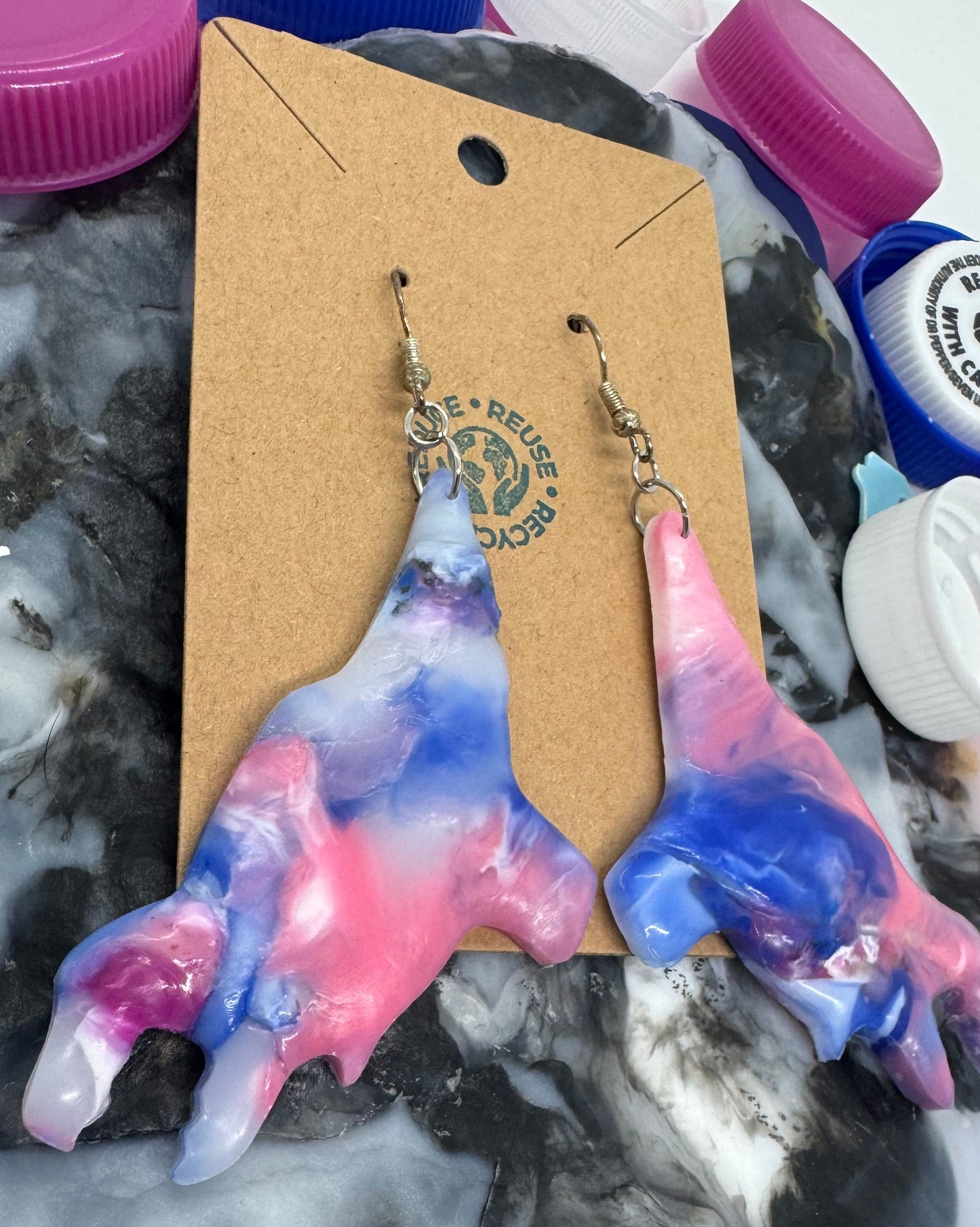 Colorful tie-dye earrings on a cardboard backing with a marbled surface background.