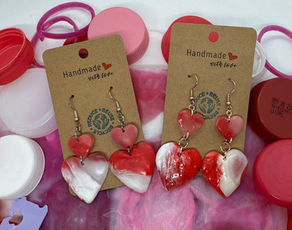 Pair of heart-shaped earrings on display with colorful bottle caps in the background.