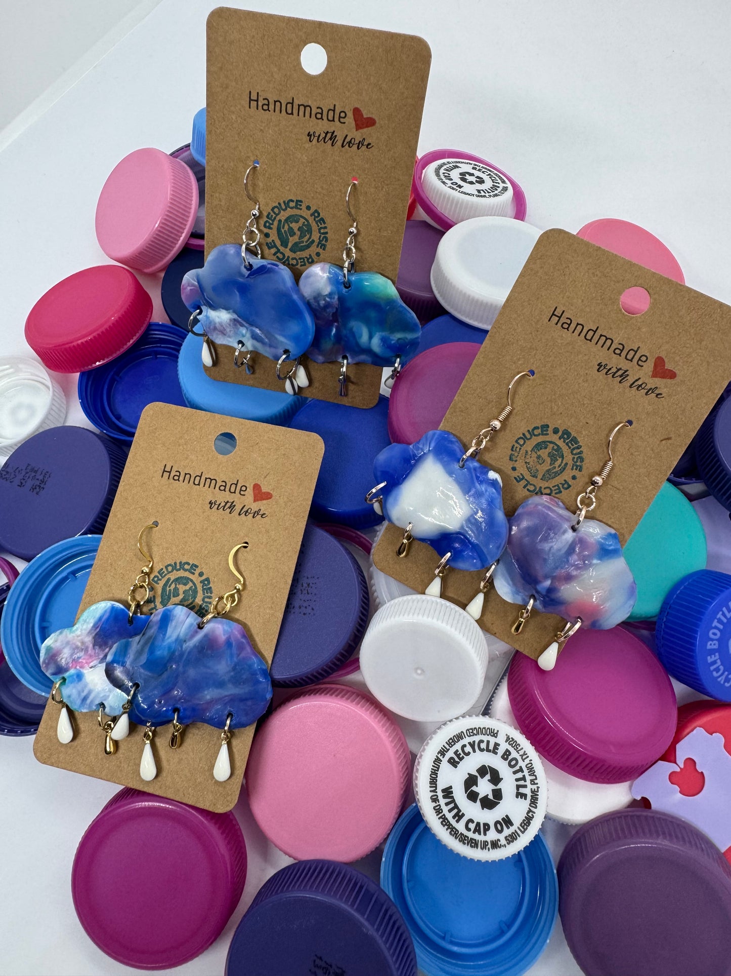 Handmade blue and white ceramic hair clips on brown cards with 'Handmade' text, surrounded by colorful bottle caps.