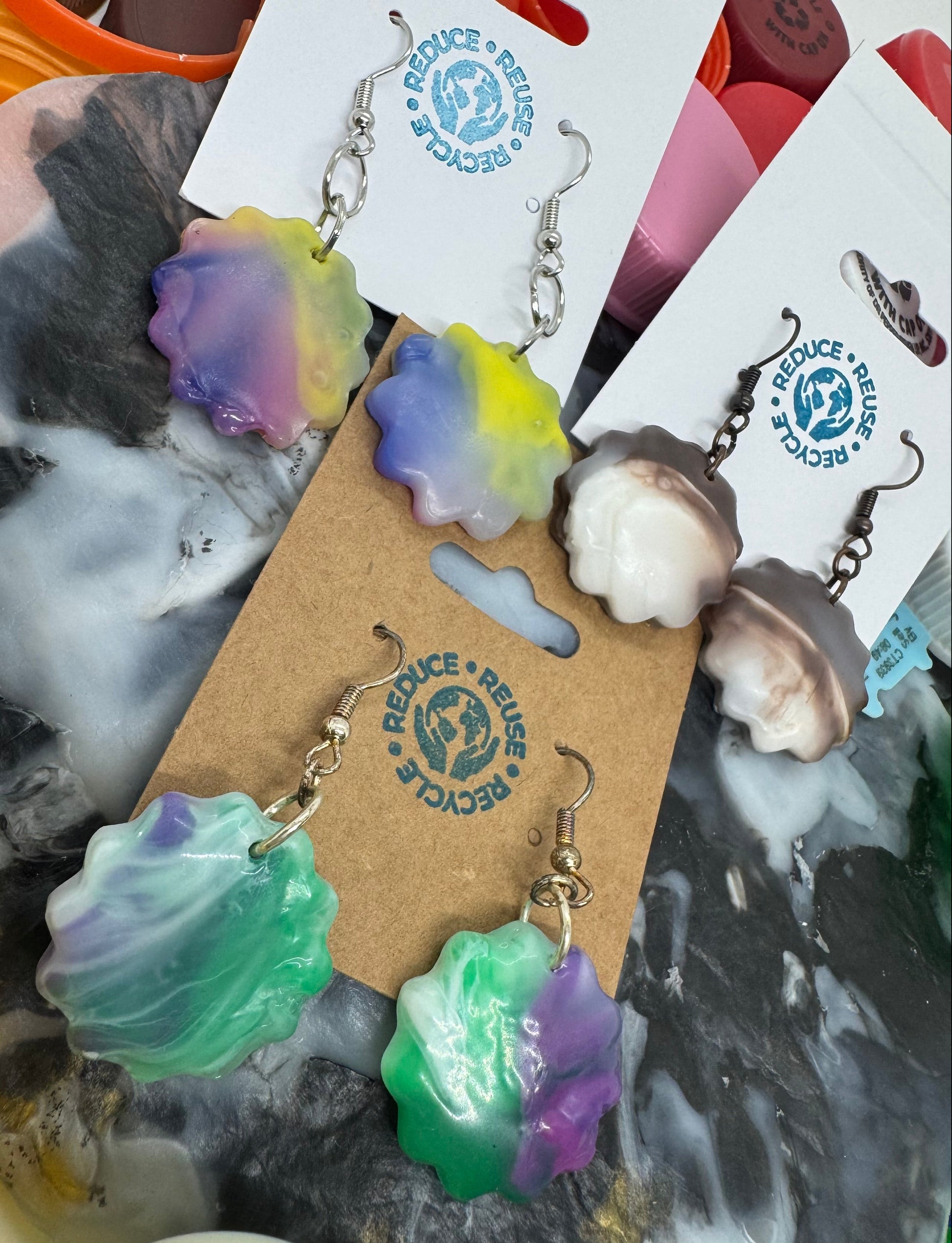 Colorful shell-shaped earrings on a marble surface with a brand card.