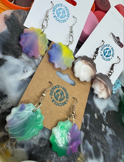 Colorful shell-shaped earrings on a marble surface with a brand card.