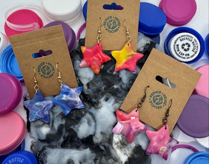 Colorful star-shaped earrings on display with various bottle caps in the background.