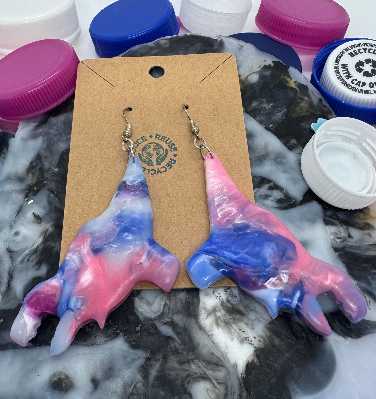 Tie-dye shark earrings on a cardboard backing with bottle caps in the background