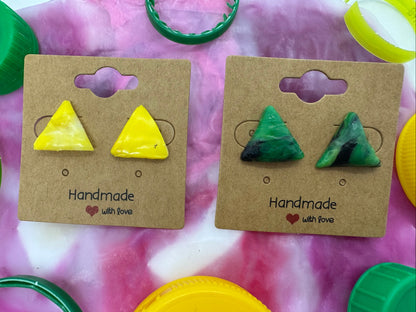 Two pairs of triangle-shaped earrings on brown cards with 'Handmade with Love' text, surrounded by colorful bottle caps.