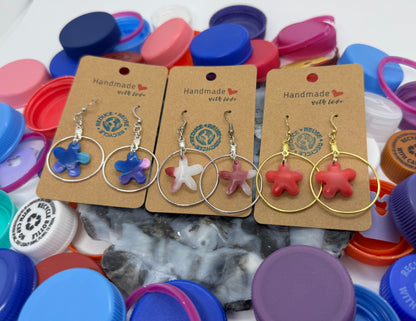 Handmade earrings on display with colorful bottle caps in the background