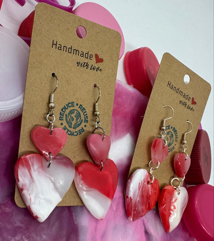 Heart-shaped earrings on a card with 'Handmade with Love' text, surrounded by pink and purple bottle caps.