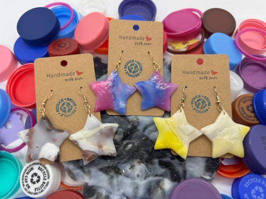 Star-shaped earrings on handmade cardboard cards with colorful bottle caps in the background.