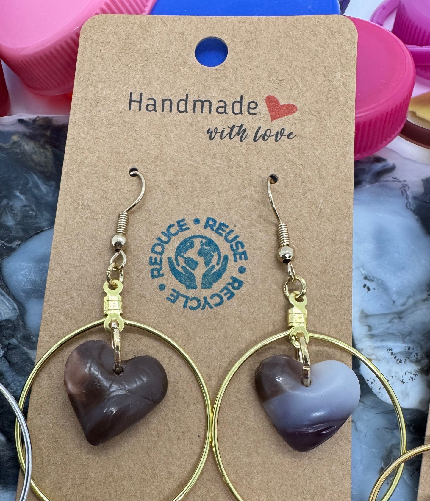 Gold hoop earrings with heart-shaped charms on a 'Handmade with Love' card, placed on a textured surface.