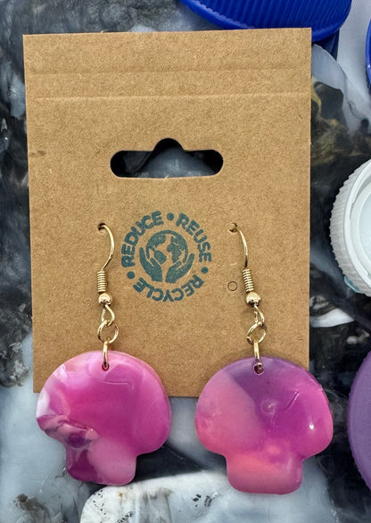 Colorful bottle caps scattered around a cardboard holder with earrings on a marble surface.