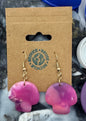 Colorful bottle caps scattered around a cardboard holder with earrings on a marble surface.