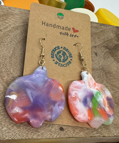 Colorful cloud-shaped earrings on a brown card with a visible brand tag, surrounded by various bottle caps.