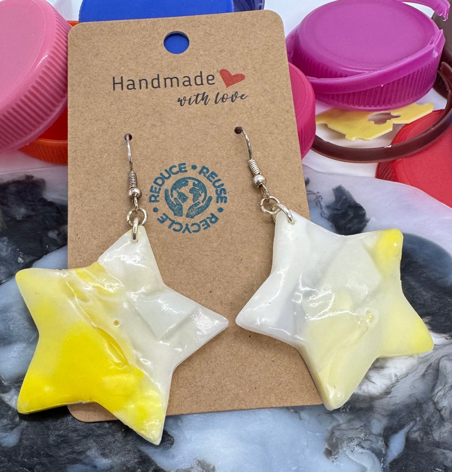 Star-shaped earrings on a card with 'Reuse Recycle' logo, placed on a textured surface.