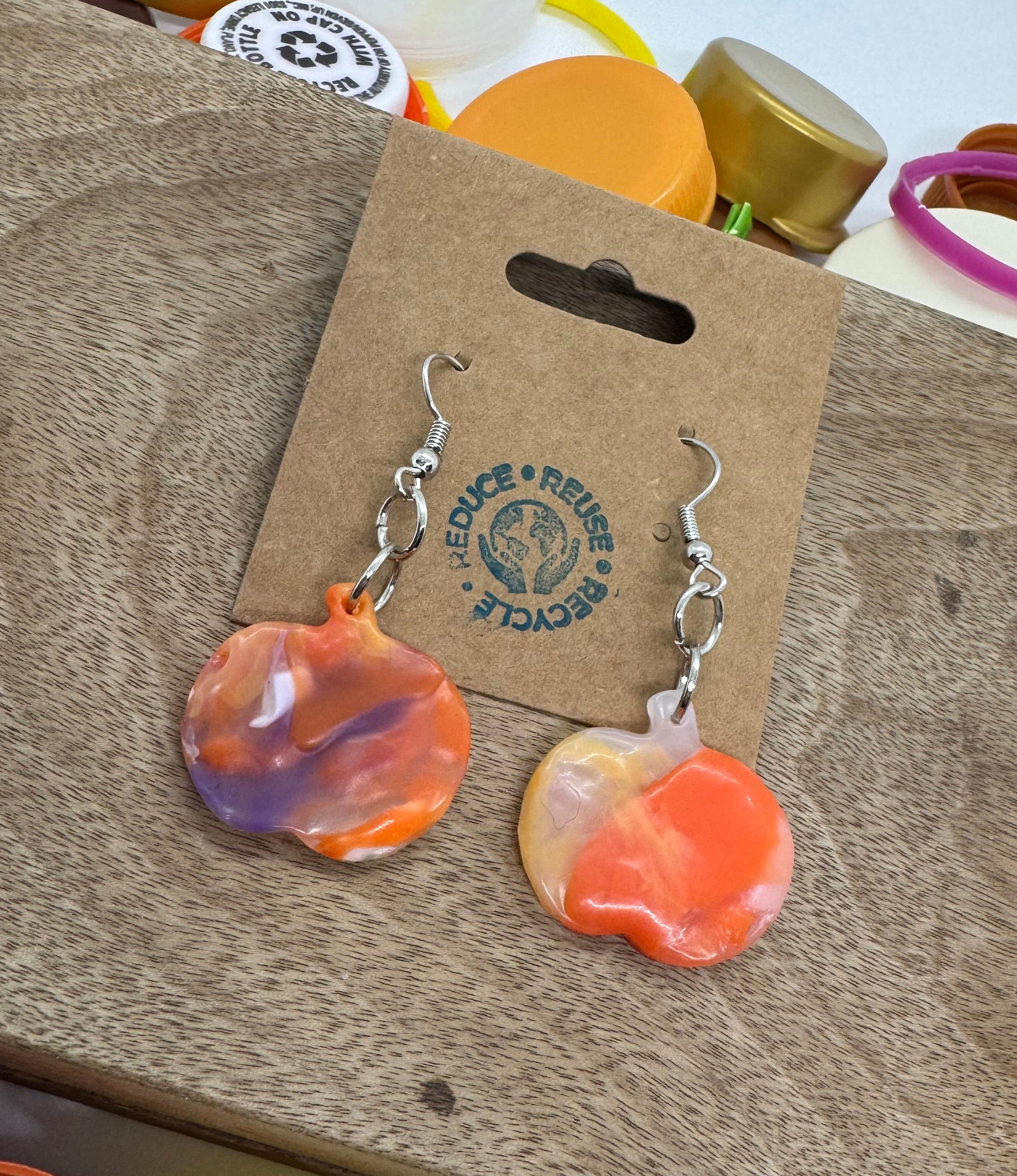 Heart-shaped earrings on a cardboard backing with a brand logo, surrounded by bottle caps.