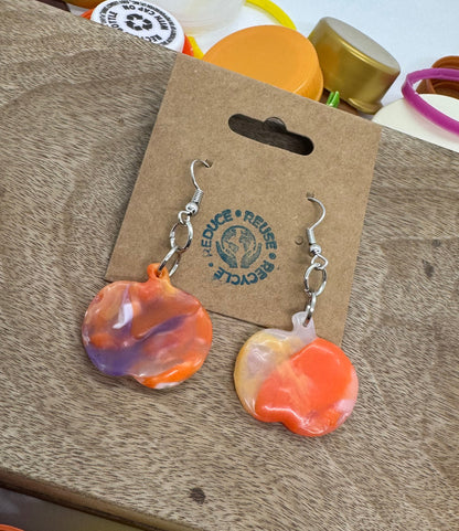 Heart-shaped earrings on a cardboard backing with a brand logo, surrounded by bottle caps.