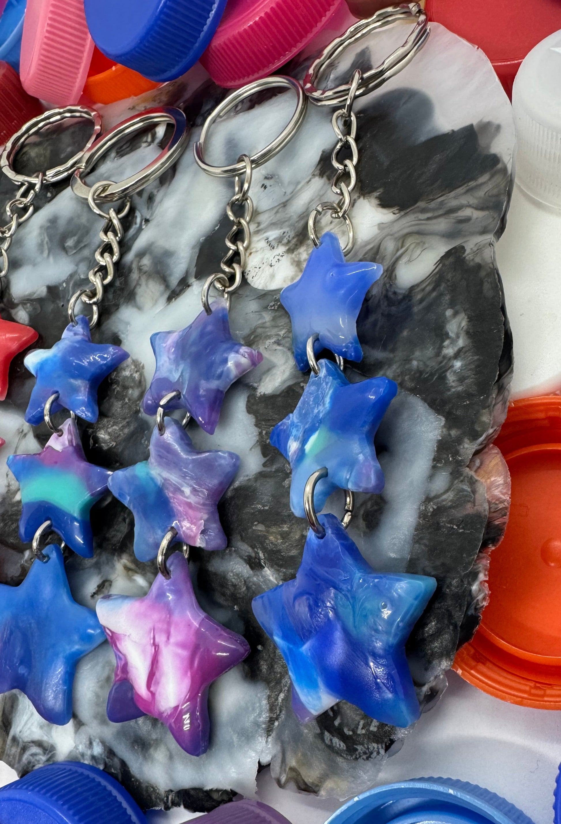 Star-shaped keychains with a chain, surrounded by colorful plastic bottle caps.