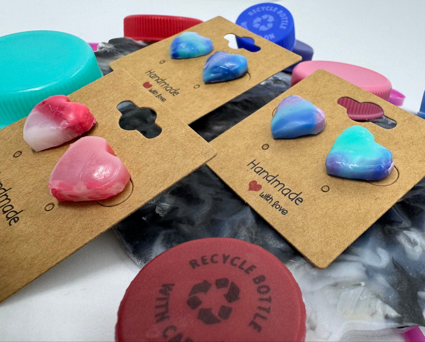 Heart-shaped earrings on cardboard cards with a recycling symbol in the background.
