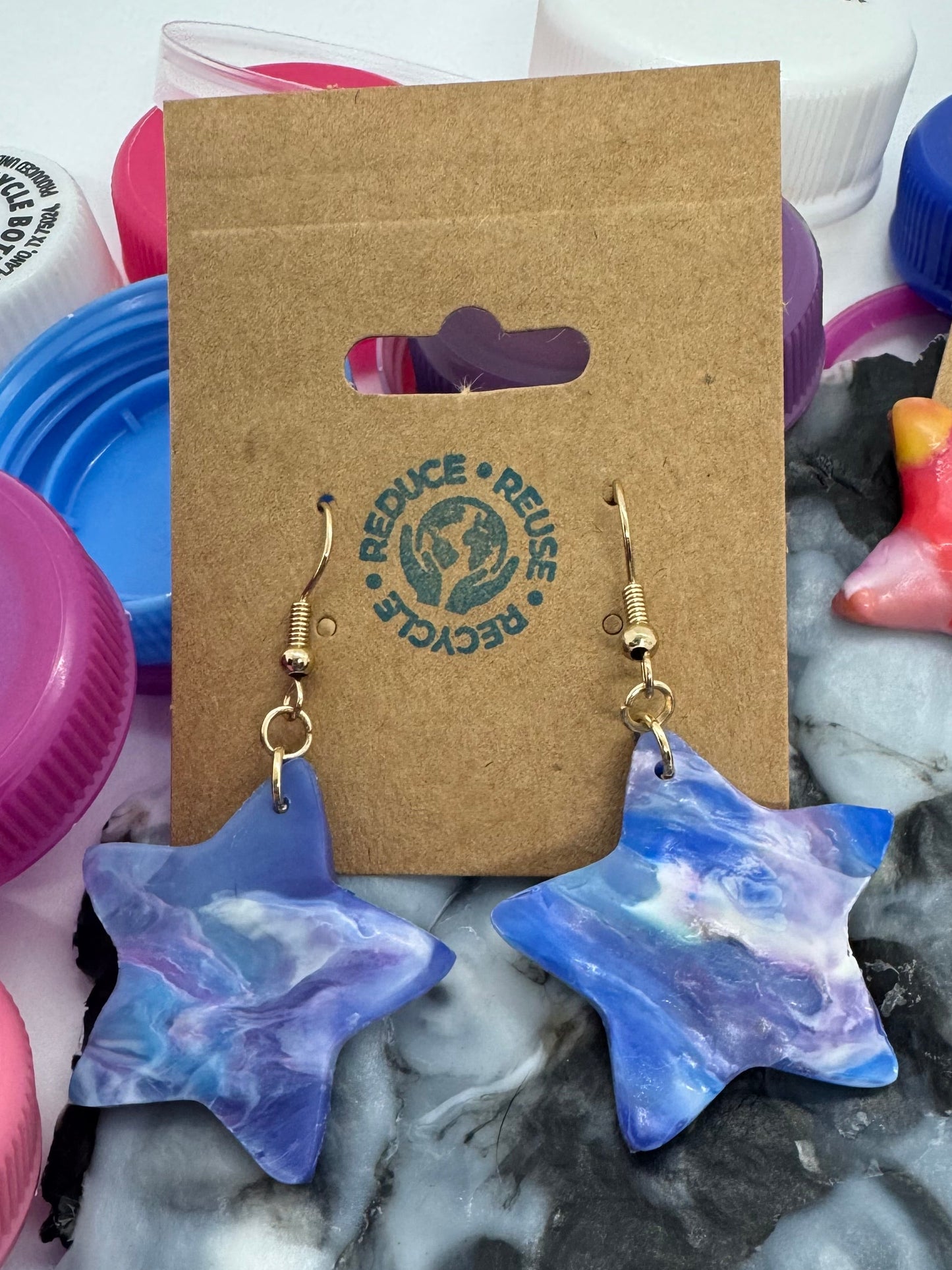 Star-shaped earrings on a card with colorful bottle caps in the background