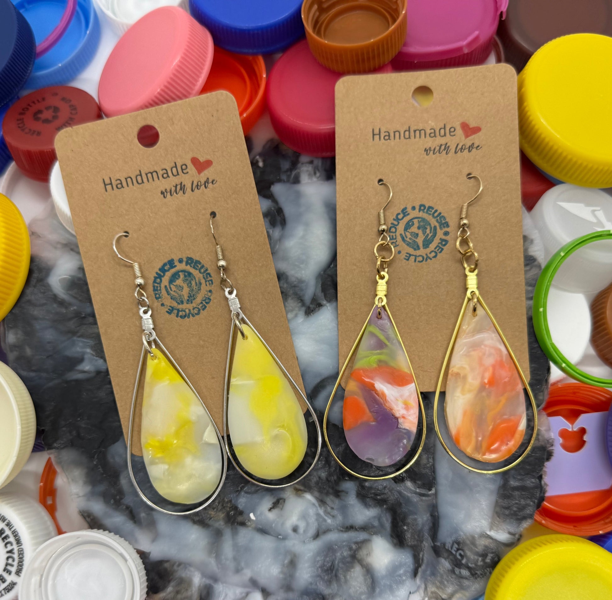 Teardrop-shaped earrings on display with colorful bottle caps in the background