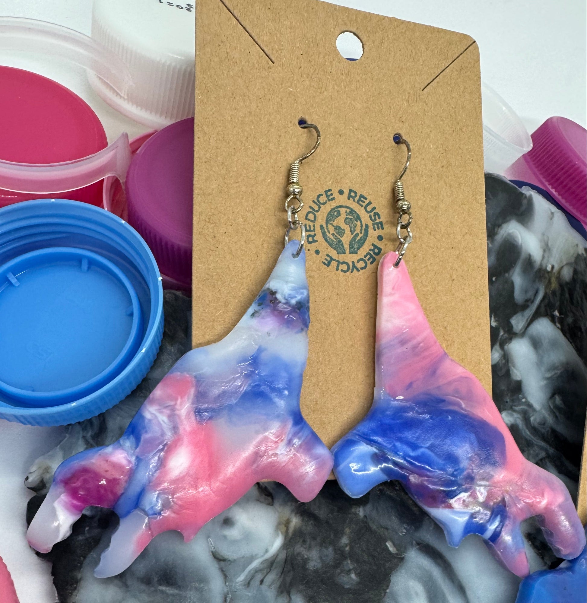 Colorful tie-dye earrings on a cardboard backing with paint containers in the background.