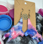 Colorful tie-dye earrings on a cardboard backing with paint containers in the background.
