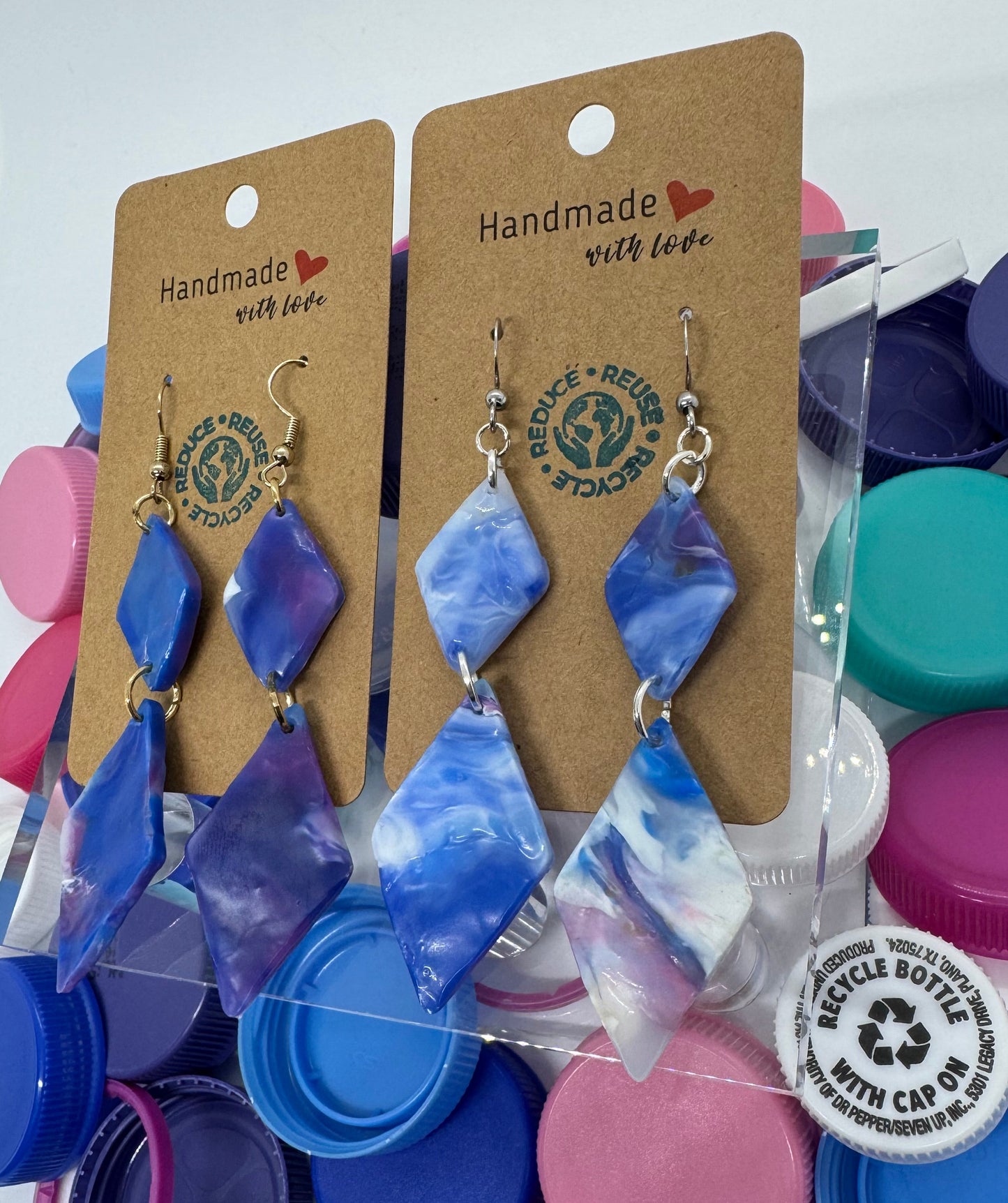 Blue and purple diamond-shaped earrings on a card with colorful bottle caps in the background.