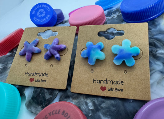 Pair of handmade flower-shaped earrings on cardboard cards with 'Handmade with love' text, surrounded by plastic bottle caps.
