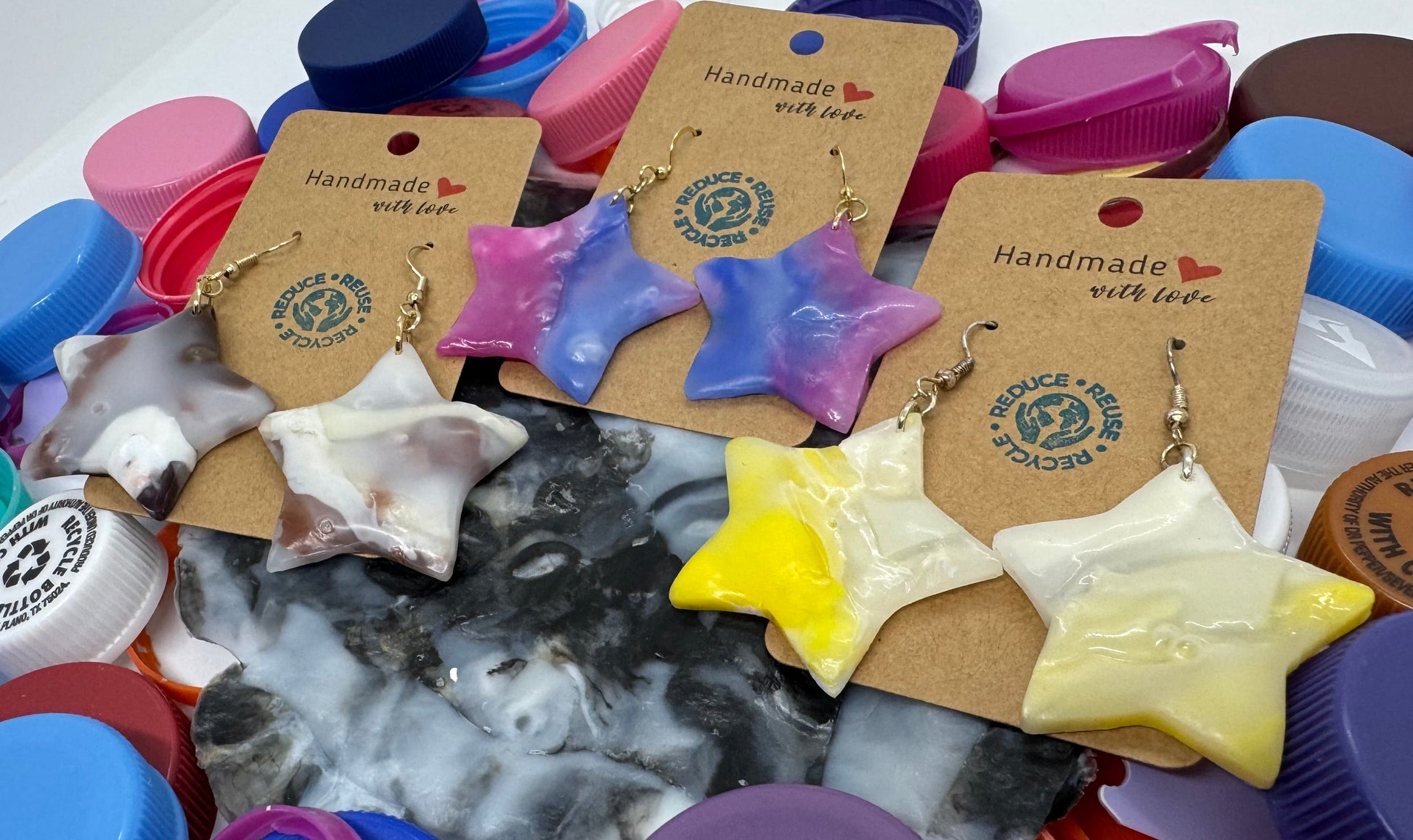 Handmade jewelry displayed among colorful plastic bottle caps on a white surface.