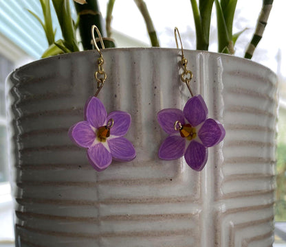 Purple flower earrings hanging from a pot with green plants in the background