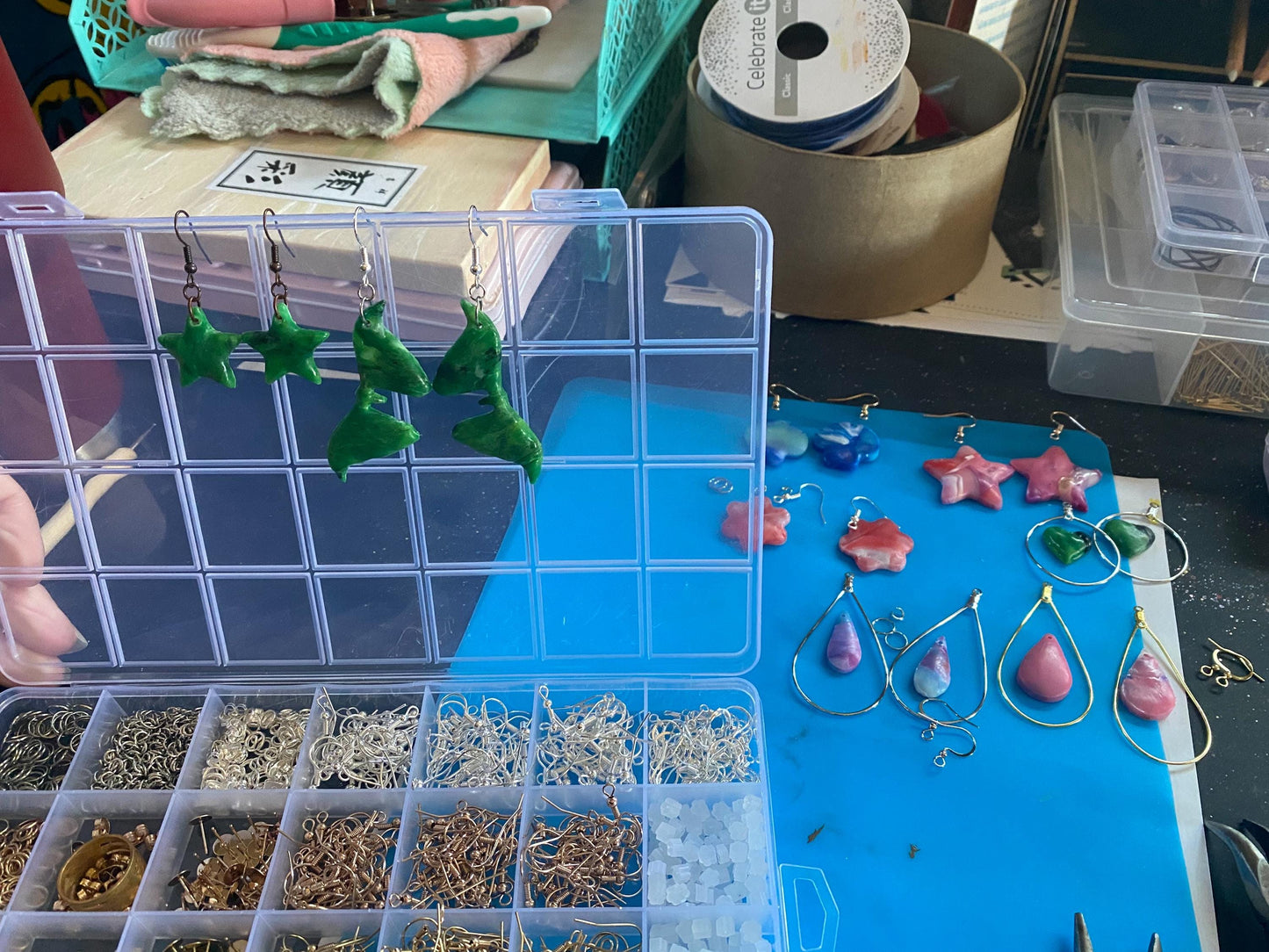 Jewelry-making setup with earrings in a clear organizer on a blue surface.