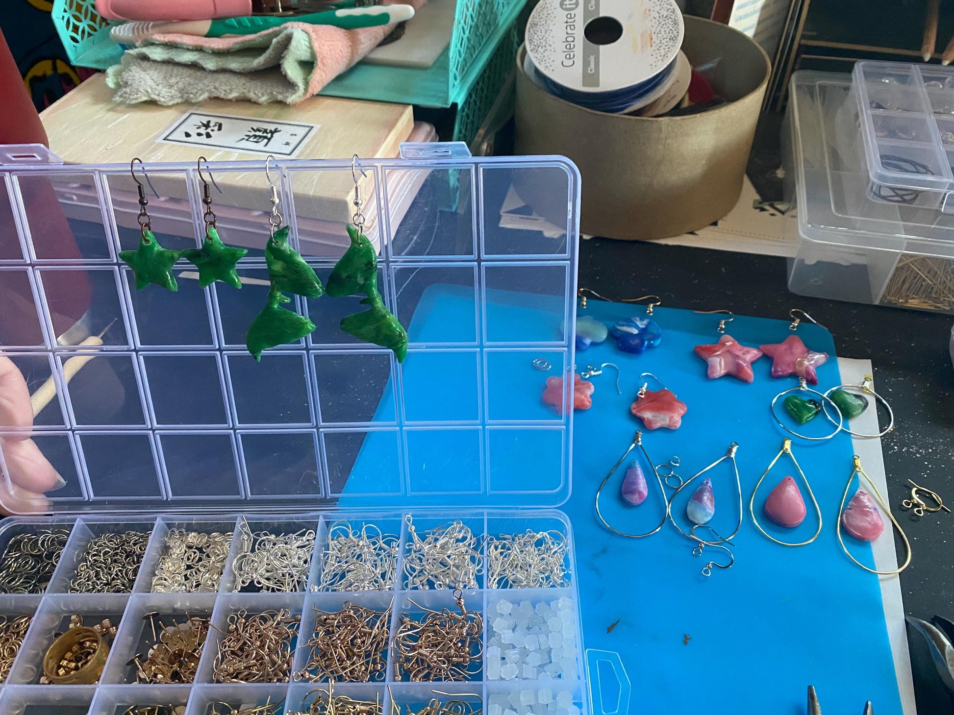 Jewelry-making setup with earrings in a clear organizer on a blue surface.