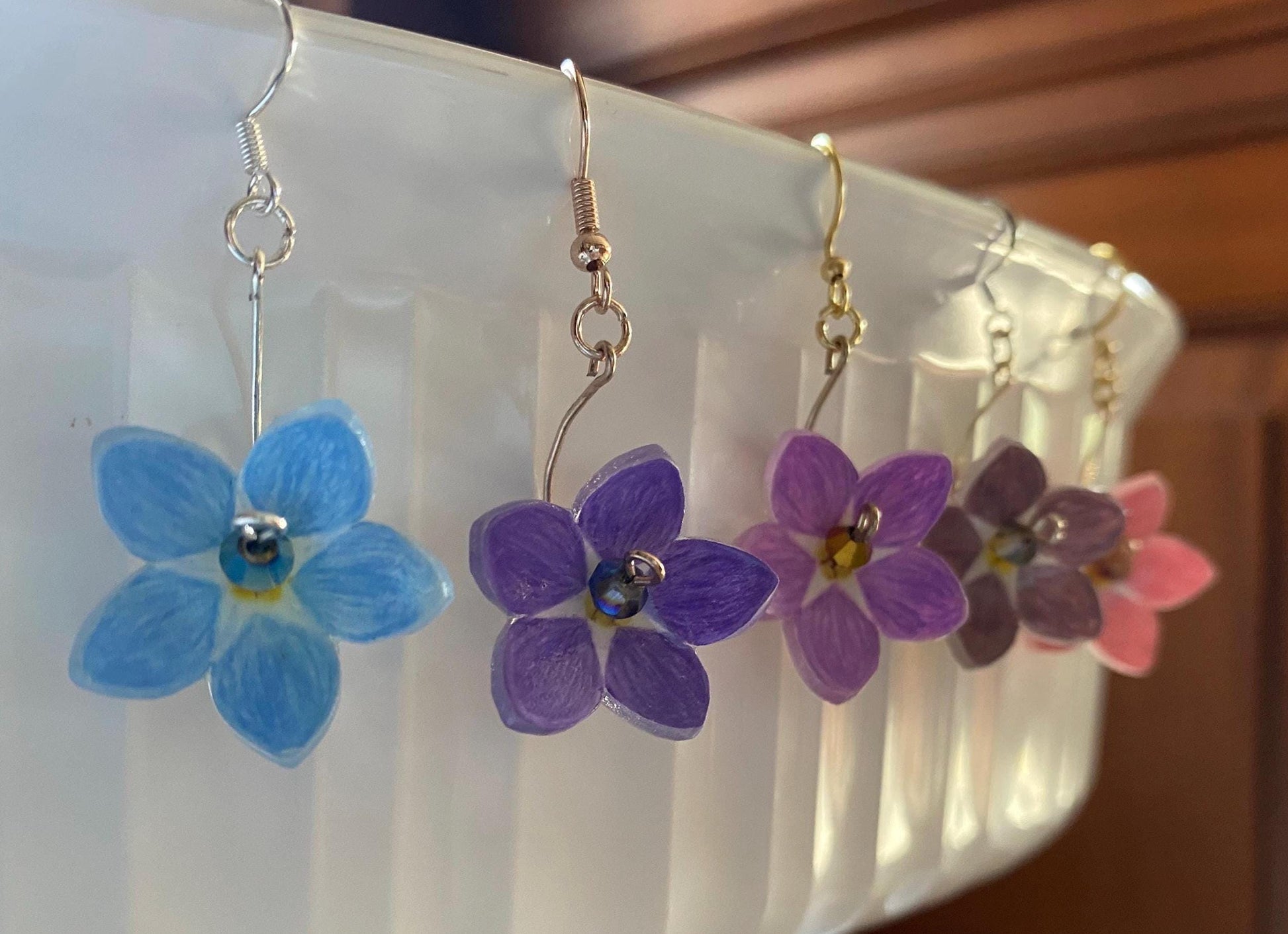 Flower-shaped earrings in blue, purple, and pink hanging on a white surface.